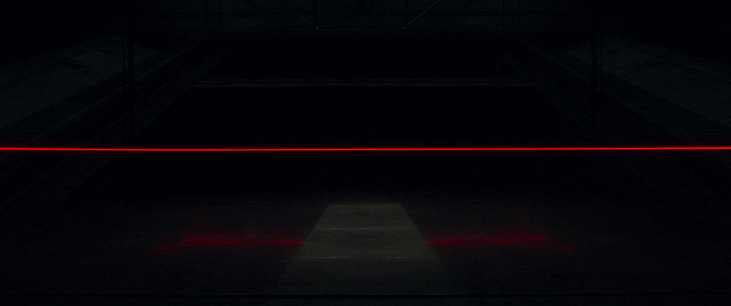 A single red line of light across a dark industrial hall